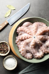 Raw octopus in bowl, peppercorns and salt on grey textured table, flat lay
