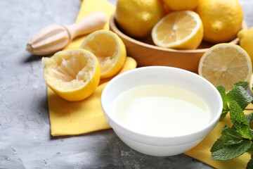 Fresh lemon juice in bowl, fruits, mint and squeezer on grey table, closeup