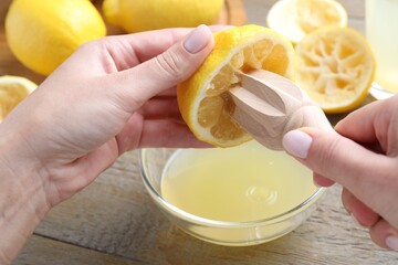 Woman juicing lemon into bowl at wooden table, closeup