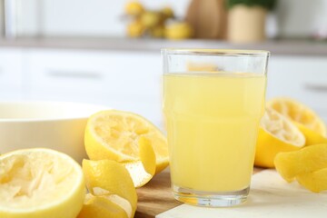 Glass of fresh lemon juice and squeezed fruits on table, closeup