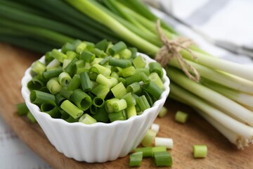 Chopped green onion in bowl and stems on table, closeup