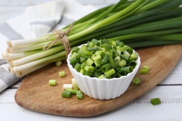 Chopped green onion in bowl and stems on white wooden table, closeup