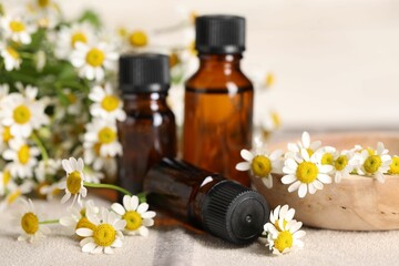 Bottles of essential oil and chamomile flowers on table, closeup