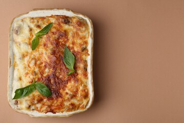 Delicious cooked lasagna in baking dish and basil on pale brown background, top view. Space for text