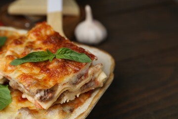 Delicious cooked lasagna with basil on wooden table, closeup. Space for text