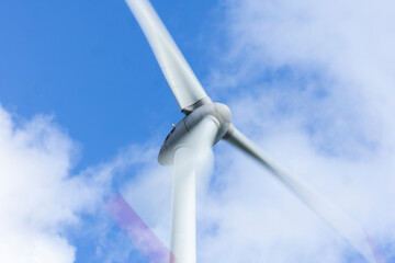 Windrad in Bewegung mit Bewegungsunsch&auml;rfe vor blauem Himmel mit Wolken