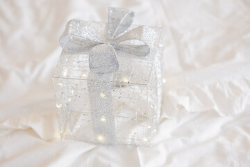Shimmering silver gift box decorated with a bow on a soft white background