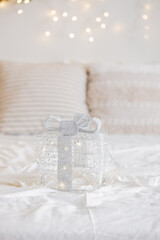 A beautiful transparent gift box with silver ribbon on a cozy bed scene