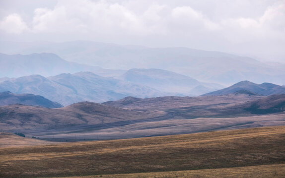 Beautiful autumn mountain landscape as a background in the steppe with dry yellow foliage, chocolate hills with haze extending into the mountains