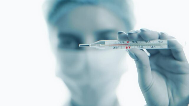 Doctor holding a mercury thermometer indicating high fever temperature 37 degrees celsius in a clinical hospital. Health care, diagnosis of illness, fever symptoms, and medical attention concept