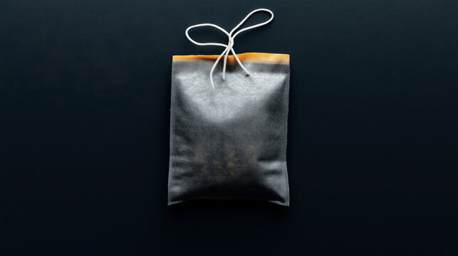 Minimalist image of a gray drawstring pouch with a white cord against a dark background, featuring an orange accent on top.