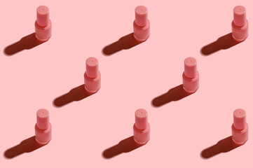 Pink glass container with nail polish on pink background.