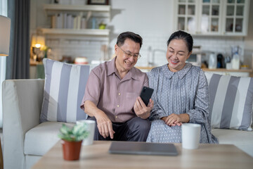 An elderly couple sits together in their cozy living room, smiling and enjoying a moment as they look at something on a smartphone. Their warmth and affection capture a peaceful home atmosphere.