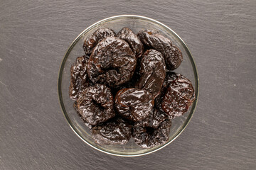 Sweet prunes in a ceramic plate on a slate stone, macro, top view.