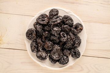 Sweet prunes in a ceramic plate on a wooden table. macro, top view.