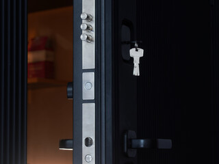 Extended door lock bolts and keys in the keyhole on an open black armored entrance door. Locking...