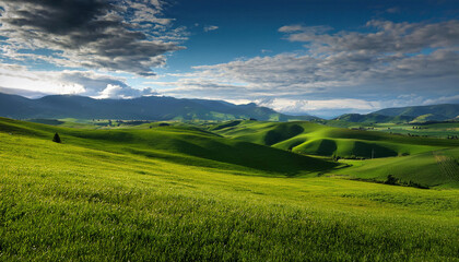 Obraz premium Rolling green hills stretch towards distant mountains under a dramatic blue sky filled with puffy white clouds.