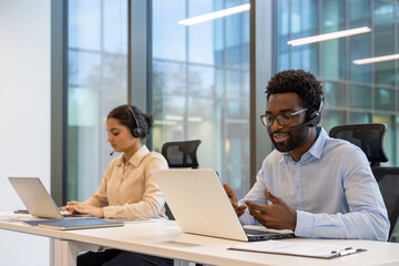 Customer support team using laptops and headsets in modern office environment. Focused on...