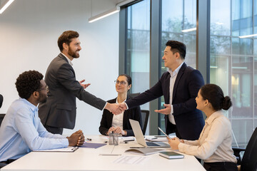 Business professionals engaged in meeting room. Two colleagues in formal attire shaking hands over...