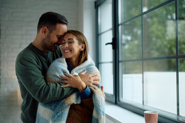 Embraced couple enjoying in cosiness of their home during cold winter day. Copy space.