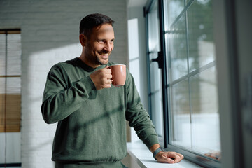 Happy man enjoying in cup of coffee by  window at home. © Drazen