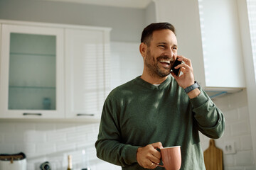 Happy man communicating on mobile phone in kitchen.