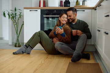 Loving couple enjoying in cup of coffee while relaxing on the floor in the kitchen.