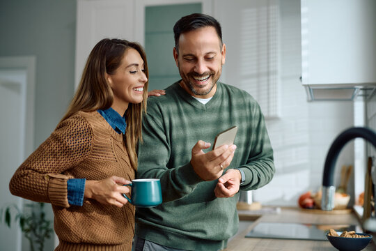 Happy couple using smart phone in kitchen.