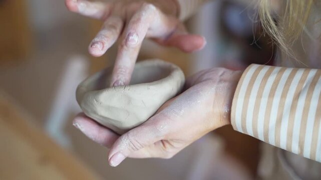 Close-up of hands working clay to form a handmade figure in a pottery workshop.
