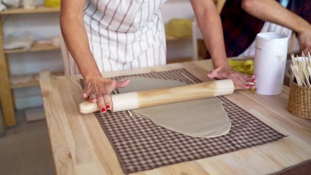 Artist rolling out clay on a textured table in pottery studio. 