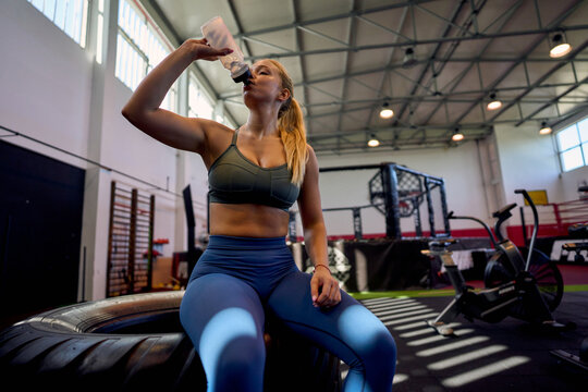Athletic female taking a drink of water during a recovery break at the gym, staying hydrated between intense workouts.
