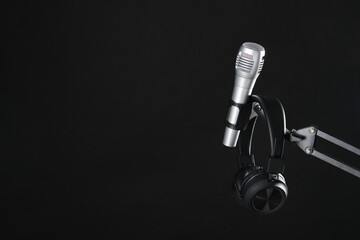 Stand with microphone and headphones on black background, space for text. Sound recording and reinforcement