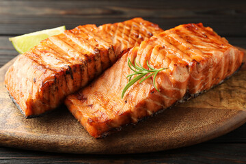 Delicious grilled salmon fillets with lime and rosemary on wooden table, closeup