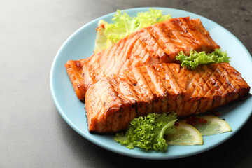 Delicious grilled salmon fillets with lettuce and lemon on grey table, closeup