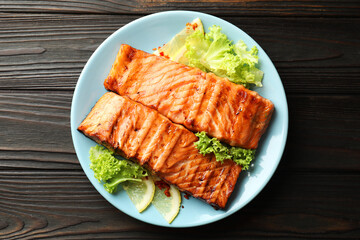 Delicious grilled salmon fillets with lettuce and lemon on wooden table, top view