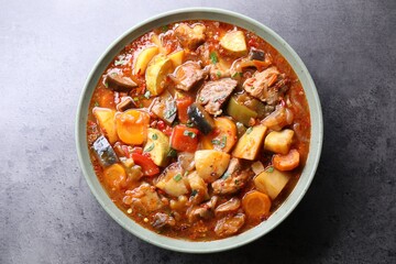 Delicious stew with vegetables in bowl on grey table, top view