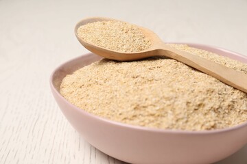 Oat bran in bowl and spoon on light wooden table, closeup