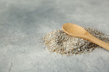 Pile of fresh rye bran and spoon on grey textured table, closeup. Space for text