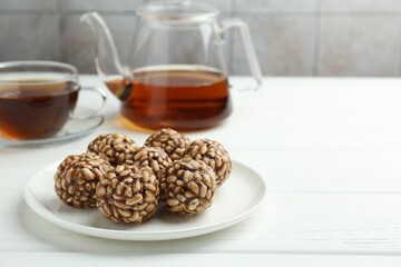 Tasty chocolate puffed rice balls and tea on white wooden table, closeup. Space for text