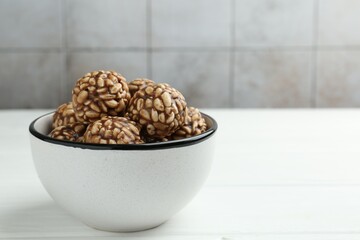 Tasty chocolate puffed rice balls in bowl on white wooden table, closeup. Space for text