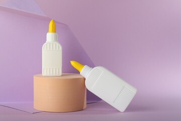 Bottles of glue and wooden podium on violet background