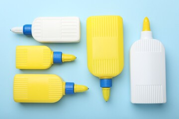 Bottles of glue on light blue background, flat lay