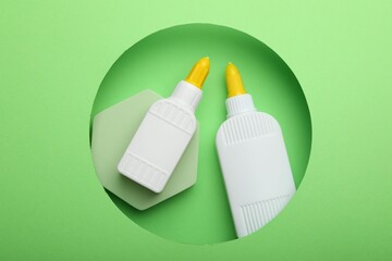 Bottles of glue on light green background, top view