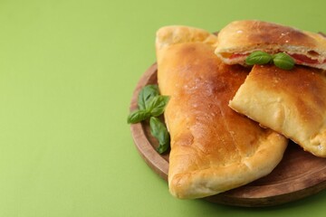 Tasty vegetarian calzones with tomato, cheese and basil on green background, closeup. Space for text