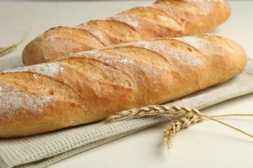 Fresh baguettes and spikes on beige table, closeup