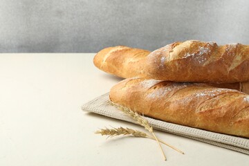 Fresh baguettes and spikes on beige table, space for text