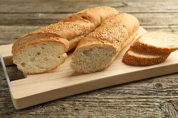 Cut fresh baguette with sesame on wooden table, closeup
