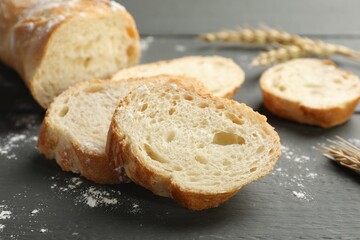 Pieces of fresh baguette with flour and spikes on grey wooden table, closeup