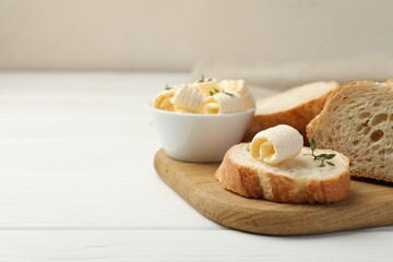 Cut baguette with butter and herbs on white wooden table, closeup. Space for text
