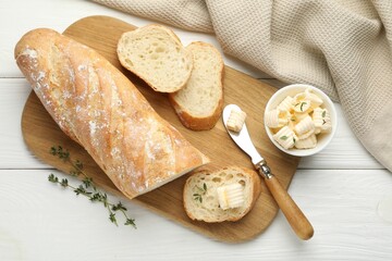 Cut baguette with butter and herbs on white wooden table, flat lay